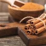 یک دسته دارچین و یک ظرف پودر دارچین در پشت آن