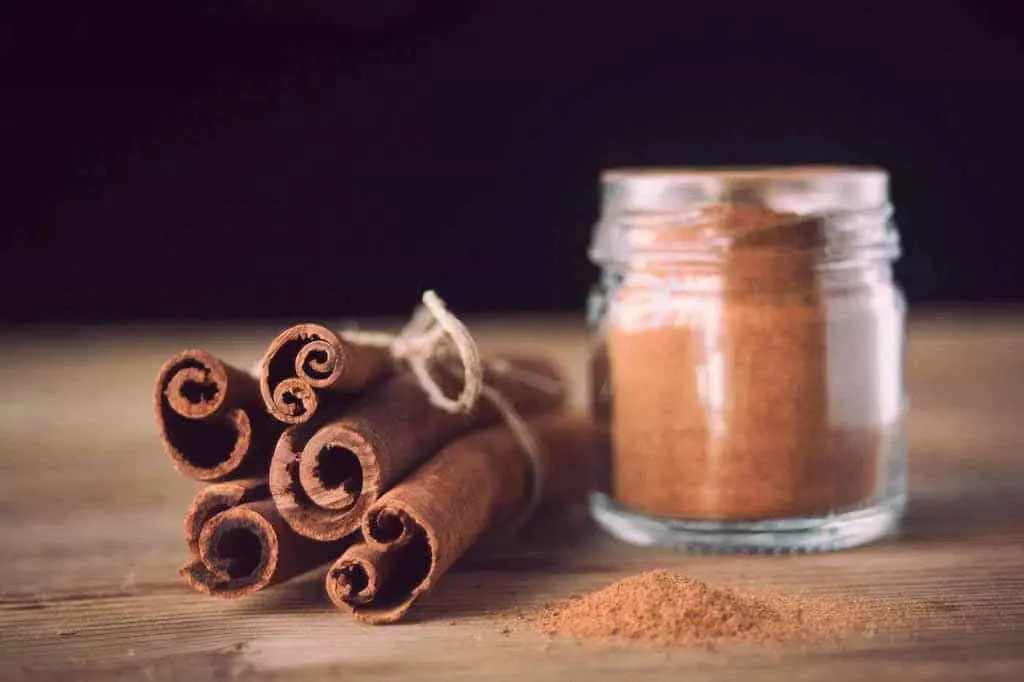 یک ظرف شیشهای دارچین آسیاب شده و یک دسته دارچین در کنارش