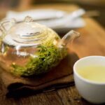 یک قوری شیشه ای حاوی چای سبز به همراه فنجان