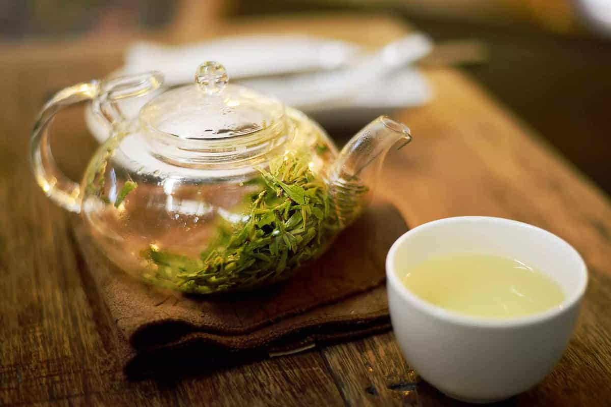 یک قوری شیشه ای حاوی چای سبز به همراه فنجان